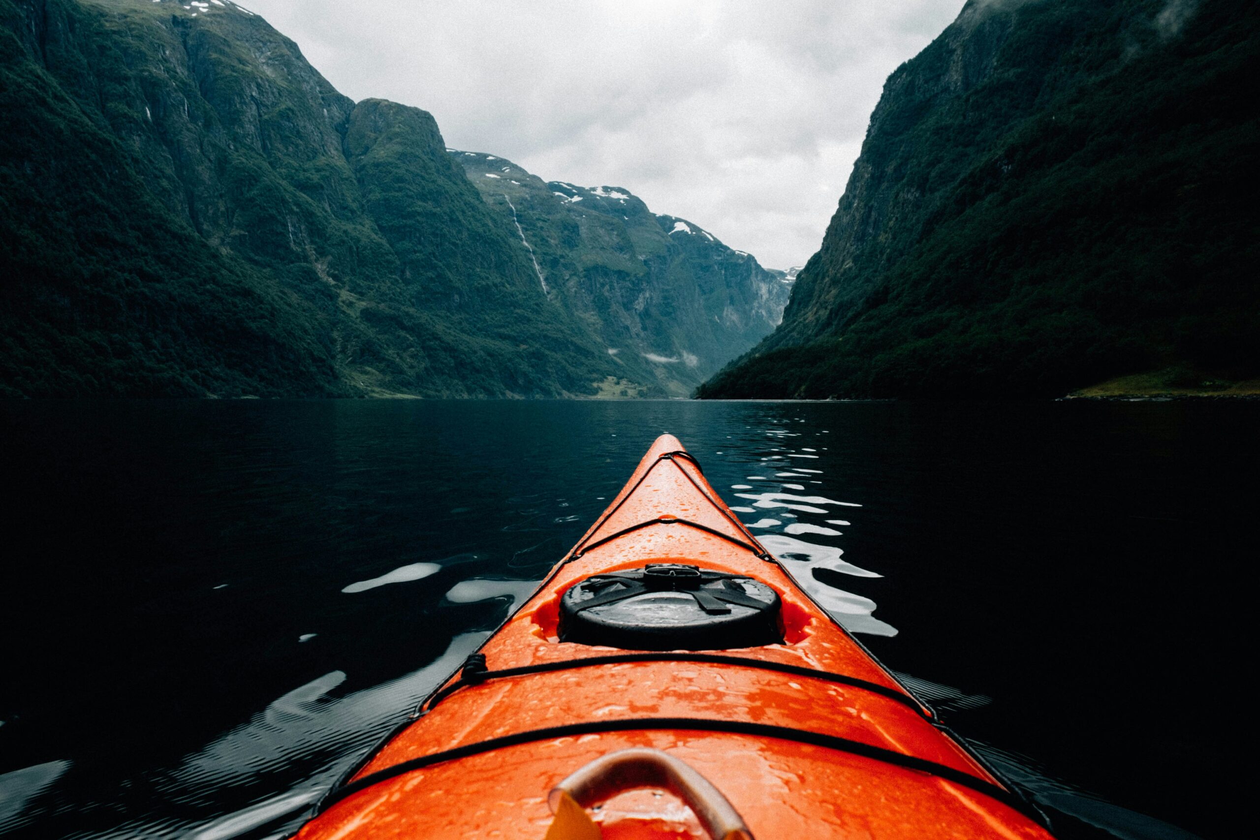 Orange kayak bow on calm water between steep green mountains